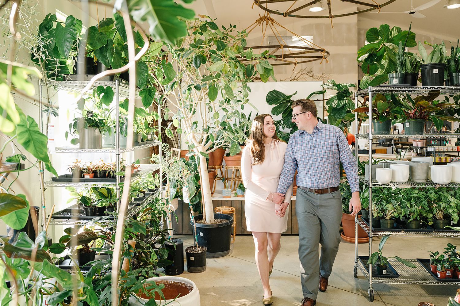 A couple walking together through a bright indoor garden center filled with tropical plants.