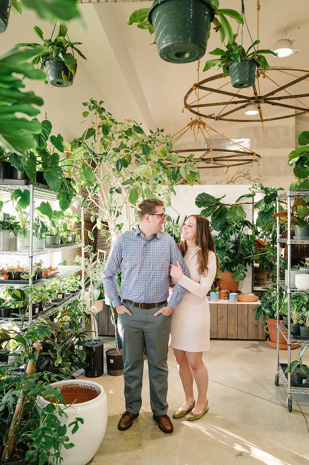 Couple shares a romantic moment in a lush indoor greenhouse filled with hanging plants and warm lighting.