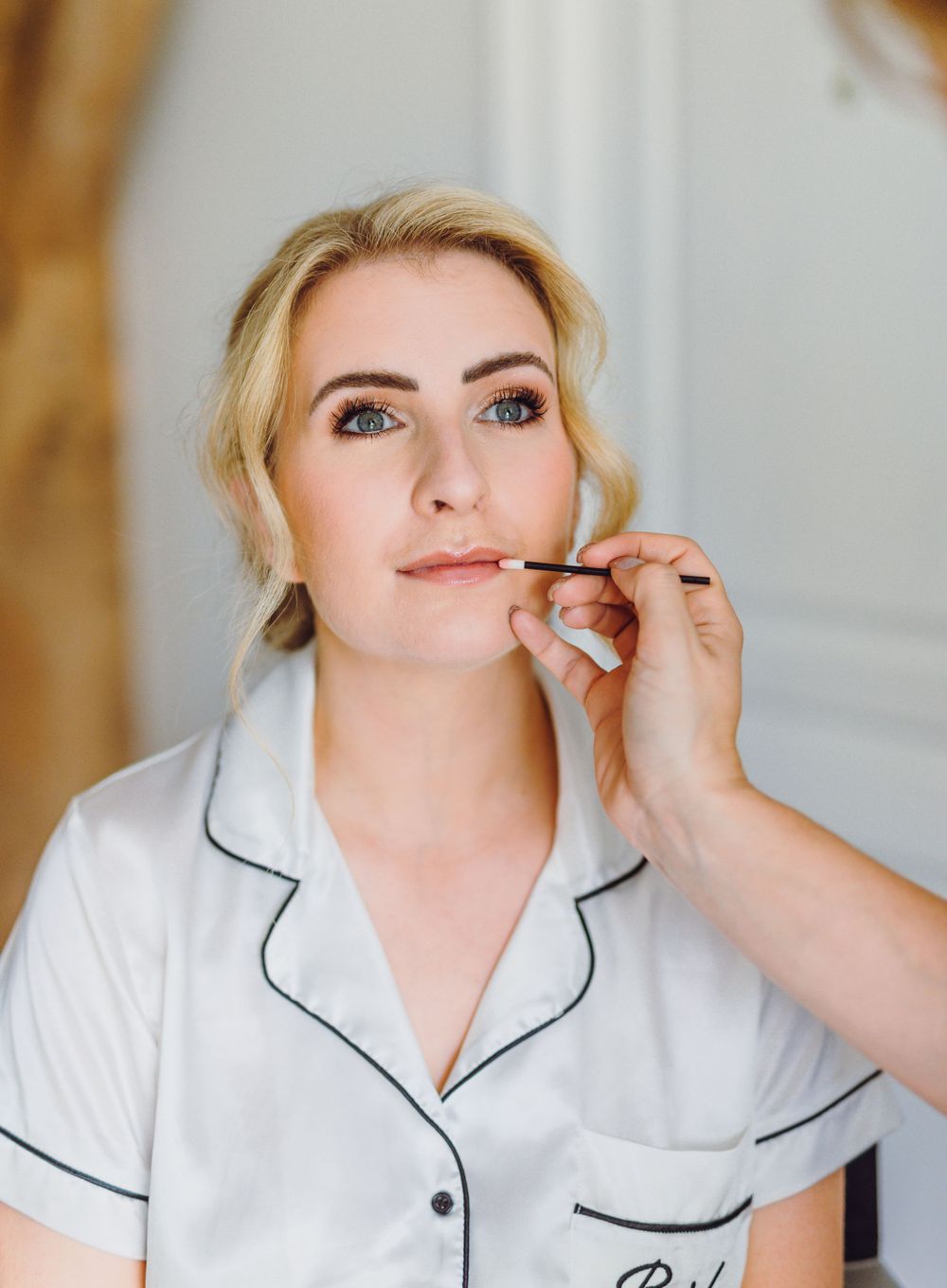 Person in white piped top getting makeup applied during preparation.