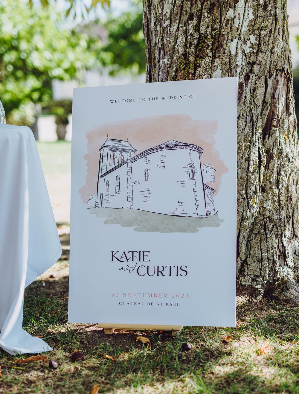Wedding program with architectural illustration displayed outdoors against tree trunk.