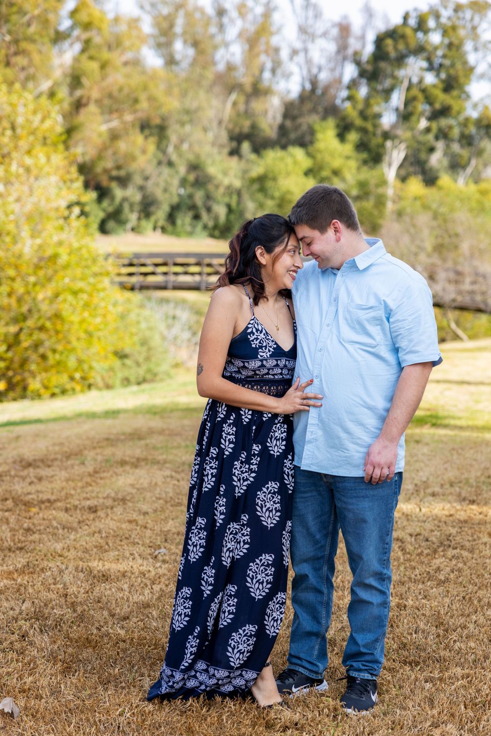 Orange County photographer captures Expecting couple laughing together in a sunny park during maternity photo session.
