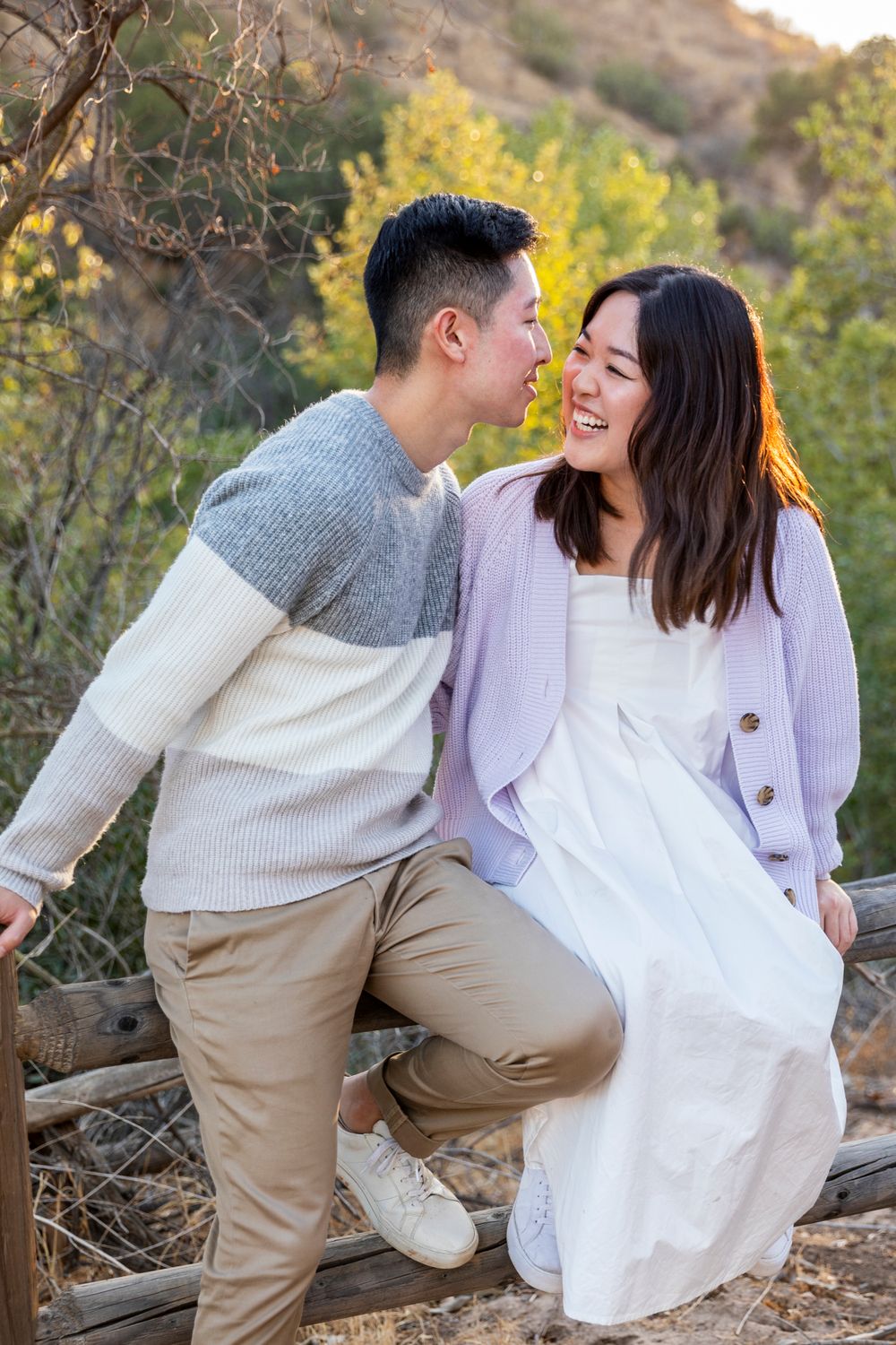 Orange County photographer captures Asian couple sharing a romantic moment sitting on a wooden fence outdoors.