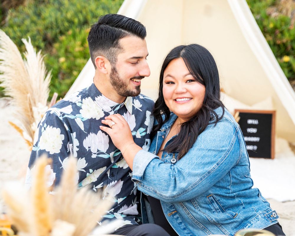 Orange County photographer captures Happy couple cuddling in front of a boho teepee setup outdoors at sunset.