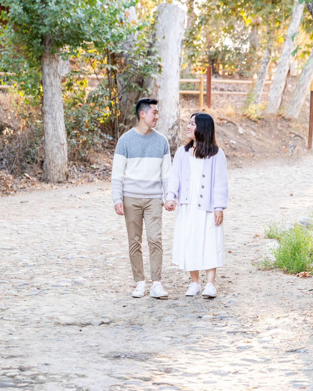 Orange County photographer captures Young Asian couple holding hands walking on a sunlit dirt path in nature.