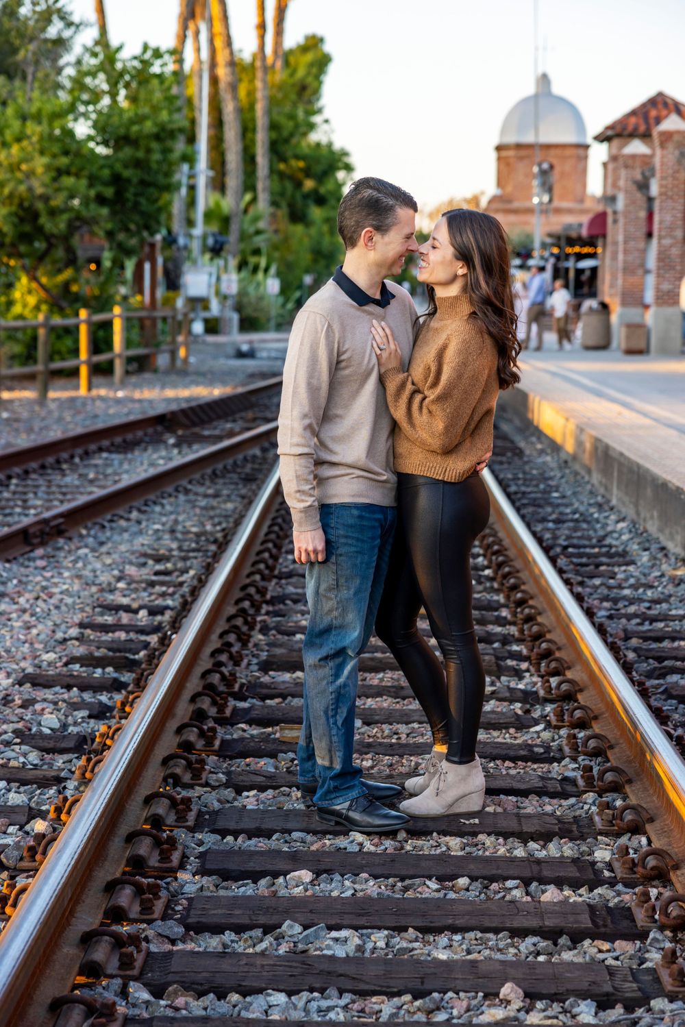 Orange County photographer captures Romantic couple nearly kissing while standing on railroad tracks at golden hour in urban setting.