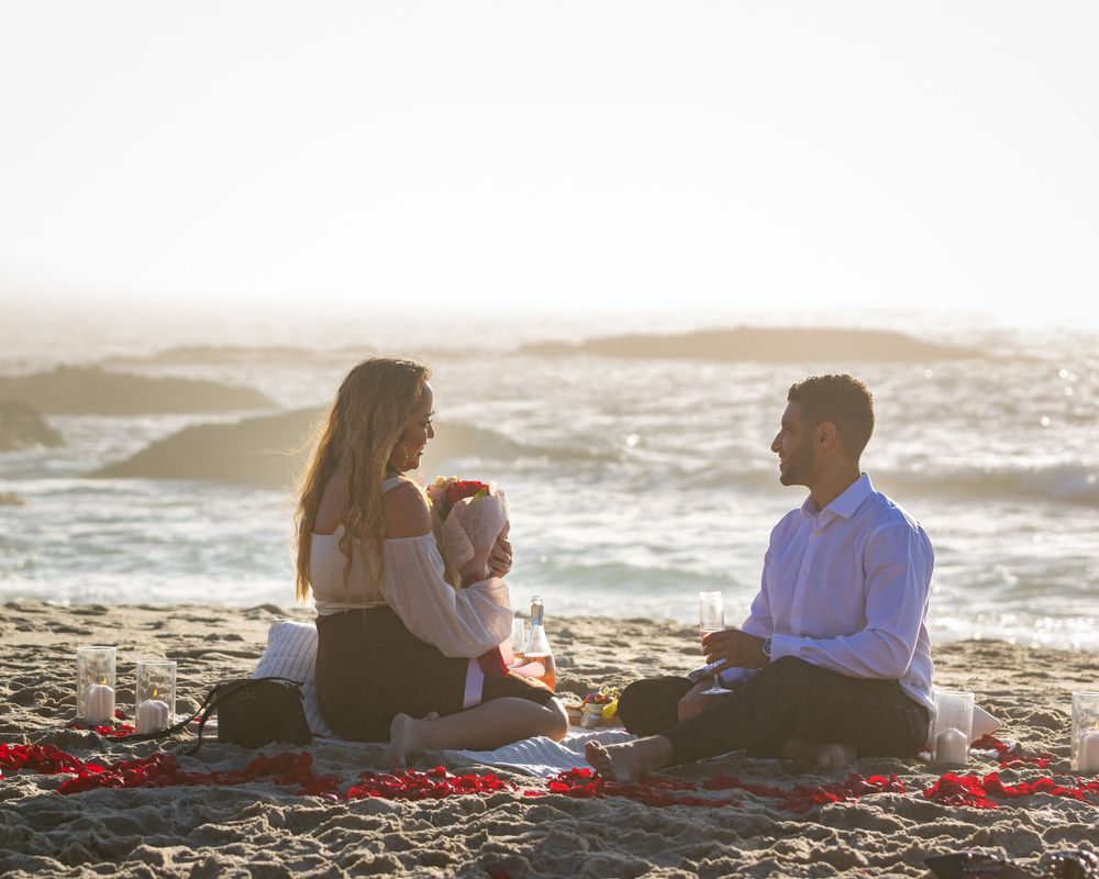 Orange County photographer captures Couple sharing a romantic beach picnic at sunset with rose petals and wine.