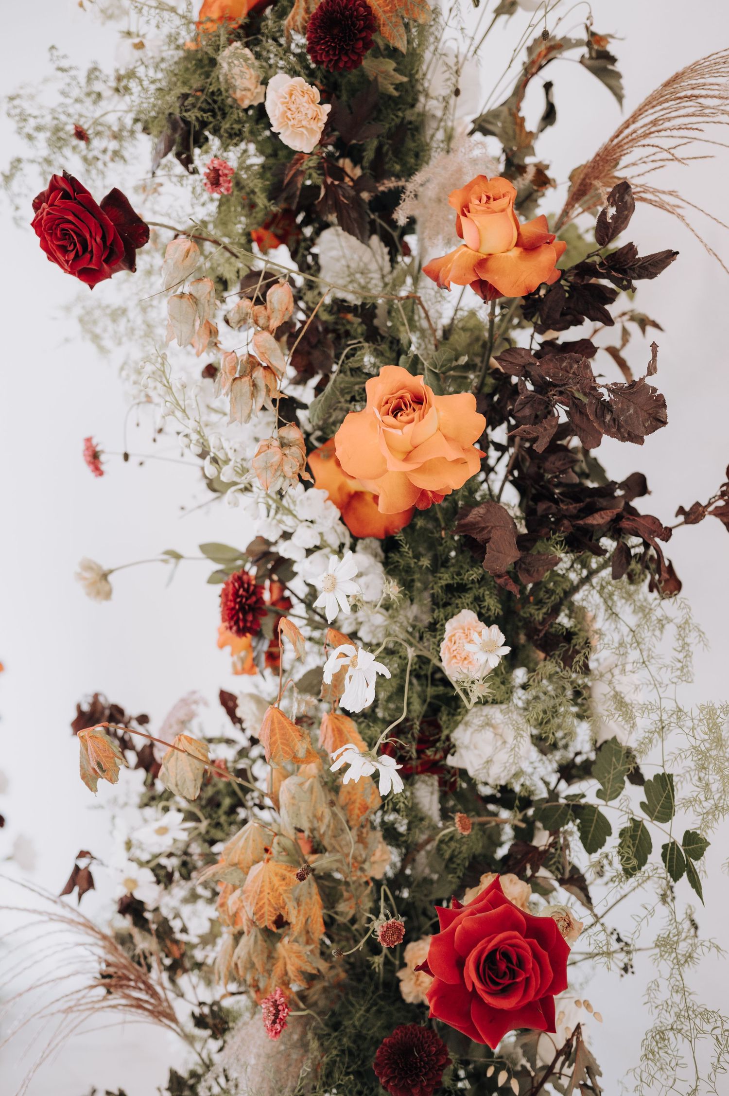 Elegant floral arrangement with orange and red roses mixed with dried flowers against white background.