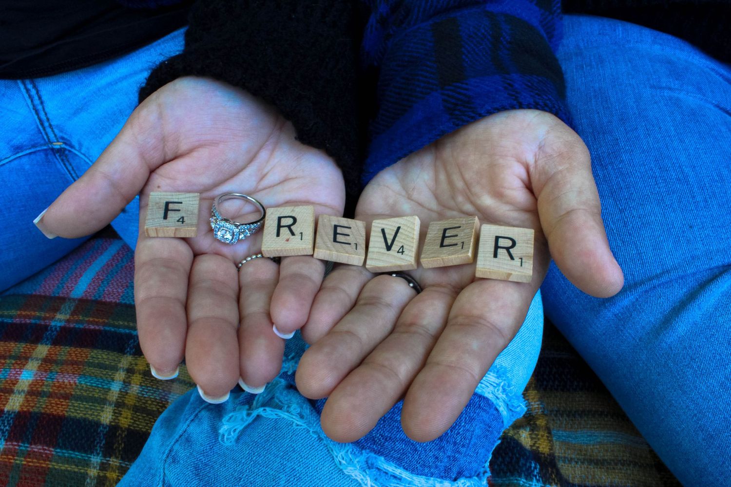 Hands holding wooden letter tiles spelling out 'FOREVER' against blue denim background.