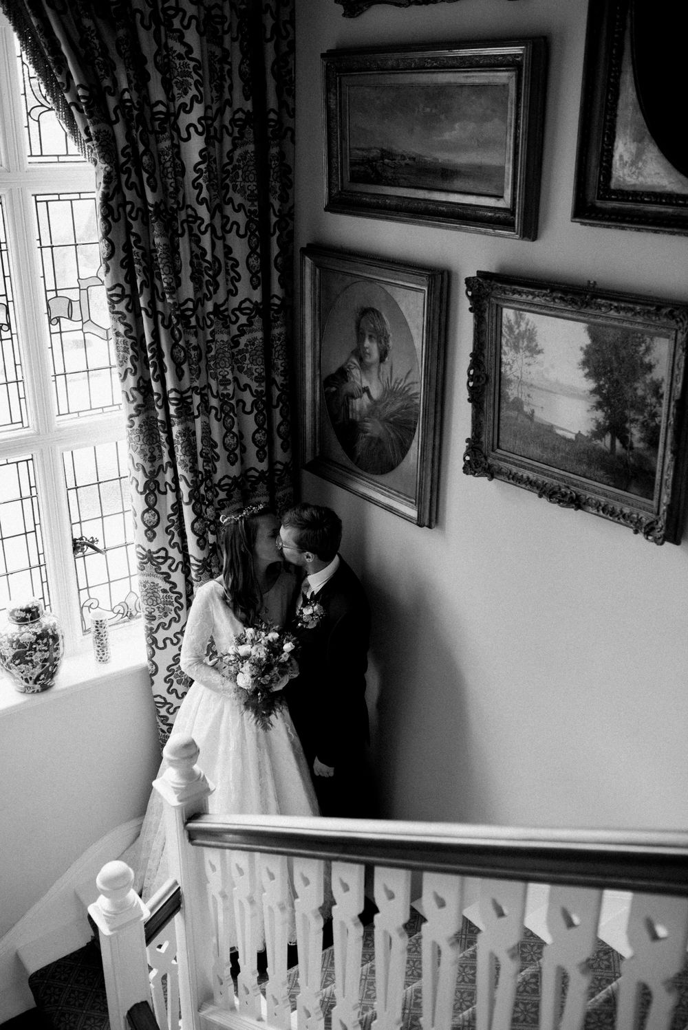 Black and white wedding photo featuring couple in a stairwell surrounded by vintage artwork.