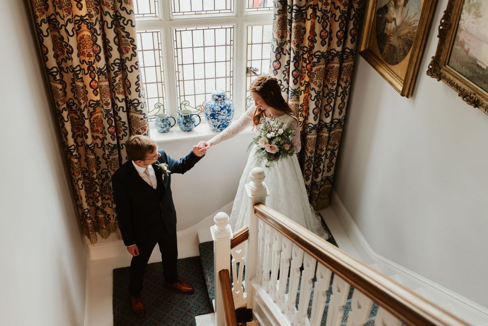 Playful wedding moment captured on an elegant staircase with decorative windows and artwork.
