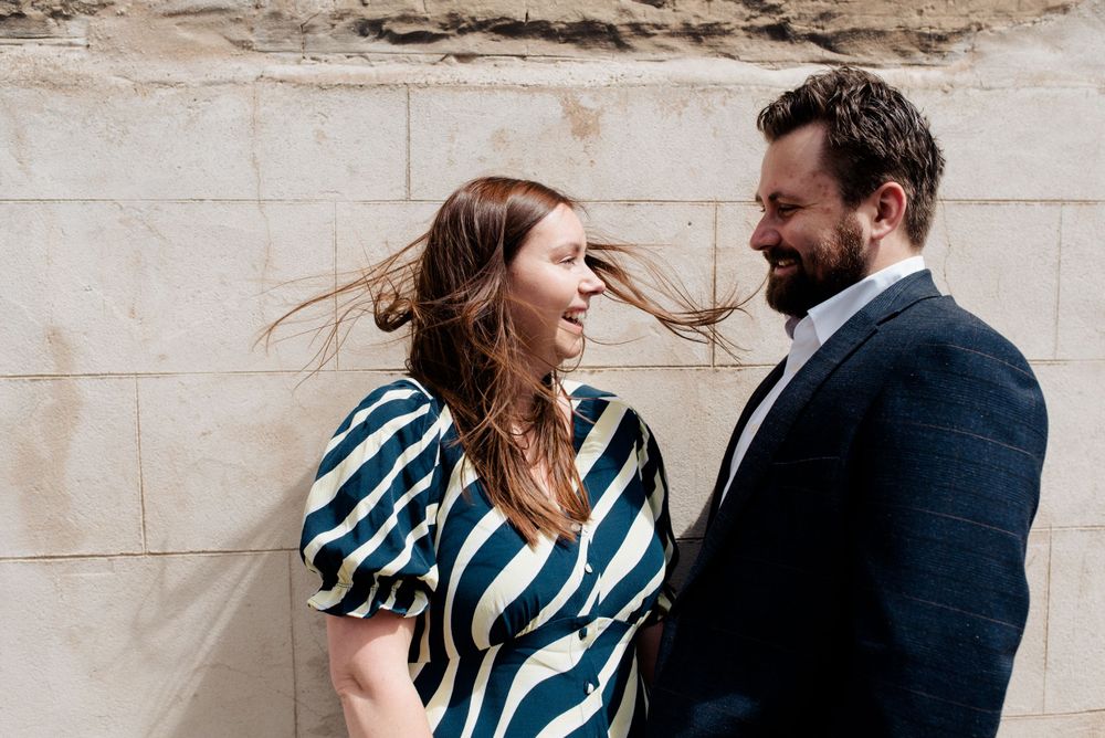 Candid moment of laughter against stone wall with wind-blown hair and striped dress.