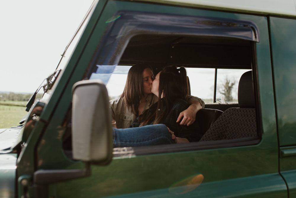 A couple sharing a tender moment inside a green vintage car on a sunny day.
