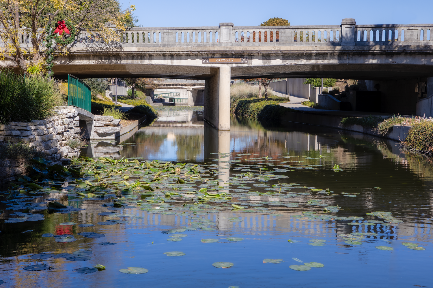 Stone bridge over canal with lily pads and reflections in blue water.