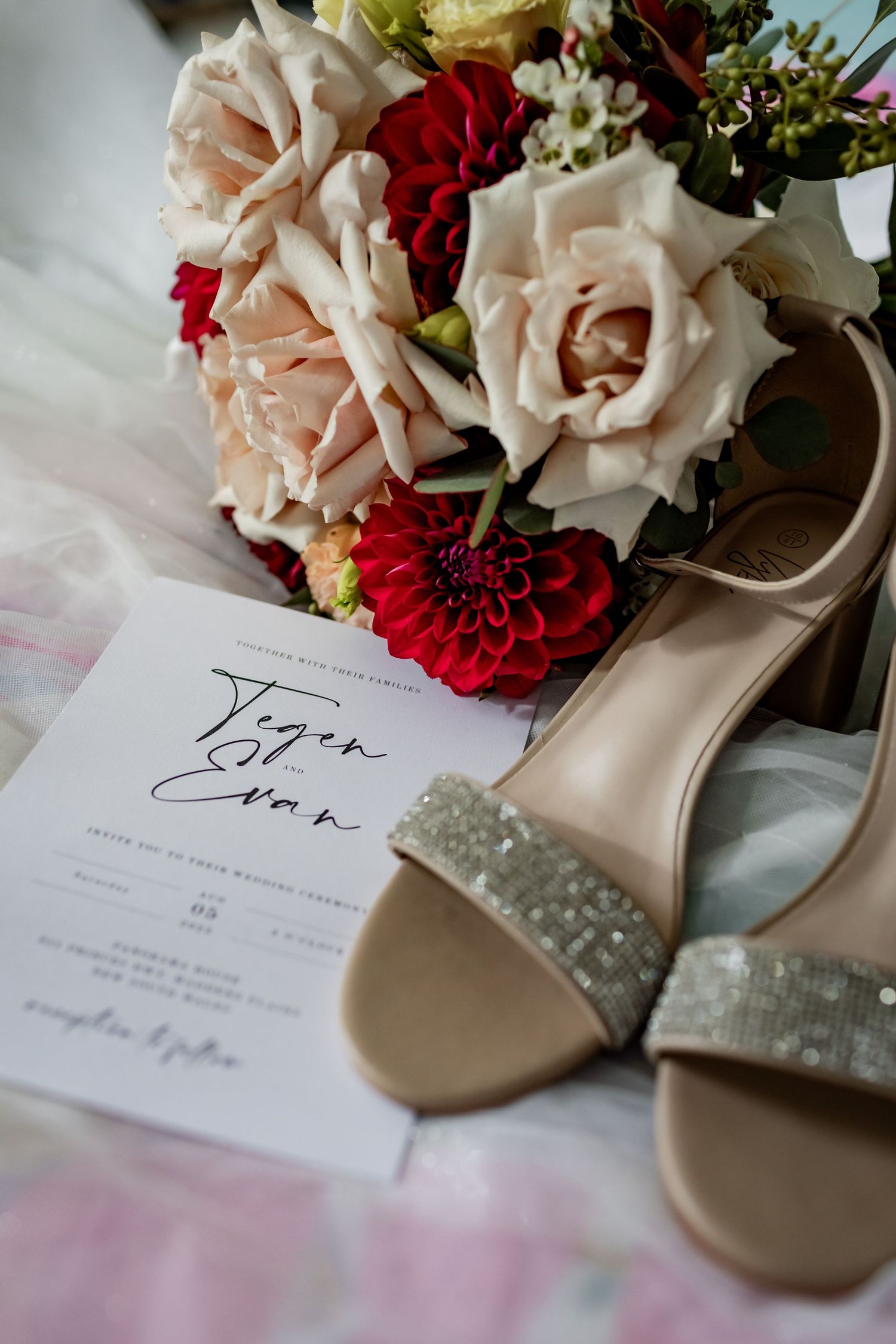 Wedding details featuring pink and red flowers, invitation, and sparkly bridal shoes.