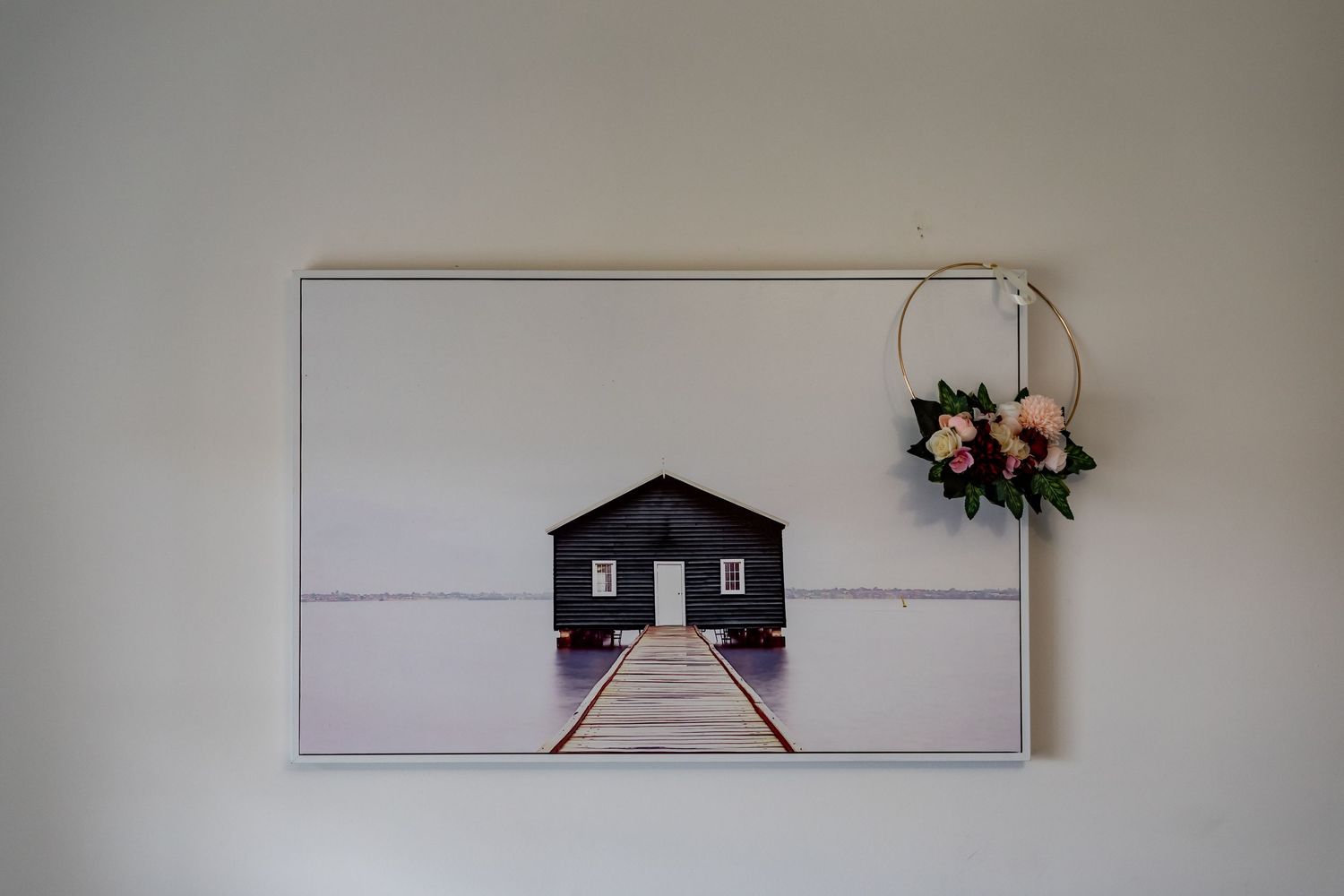Minimalist wall art featuring a black boathouse on a pier with floral accent decor.