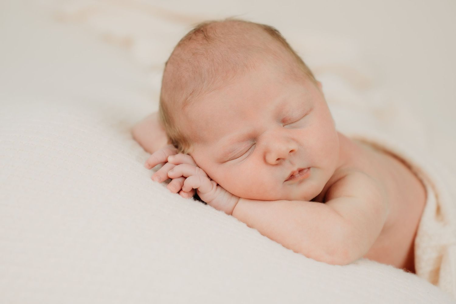 Peaceful sleeping newborn with hands under cheek on cream background.