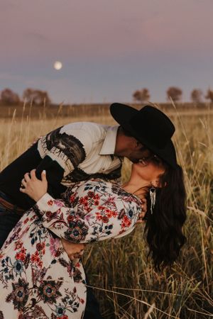 Cowboy dips fiance in a prairie field with harvest moon behind them