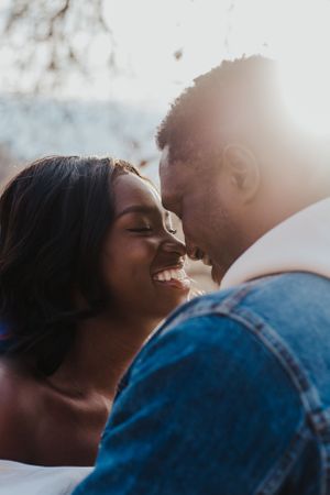 couple smile while noses touch and sunsets behind them