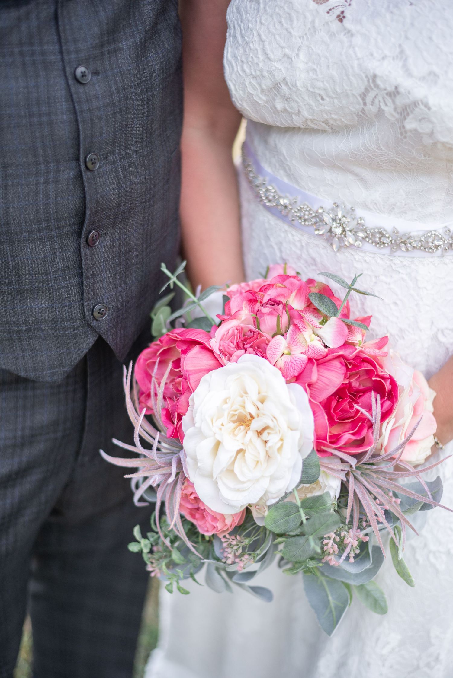 Bride and groom standing side by side with camera zoomed in on her bridal flowers she's holding between them.