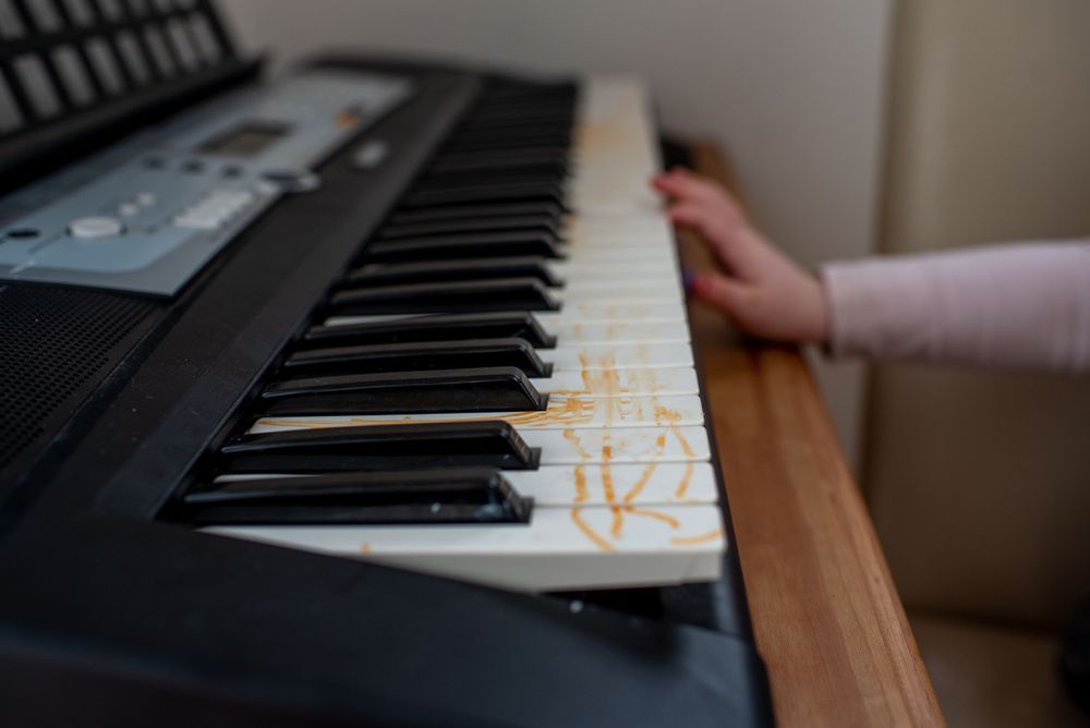 Close-up view of electronic keyboard keys with someone's hand resting on wooden surface.