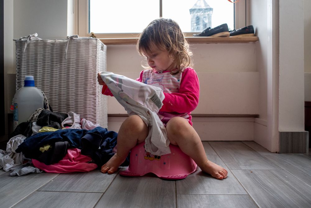 Small child in pink sitting on a pink potty seat while reading.