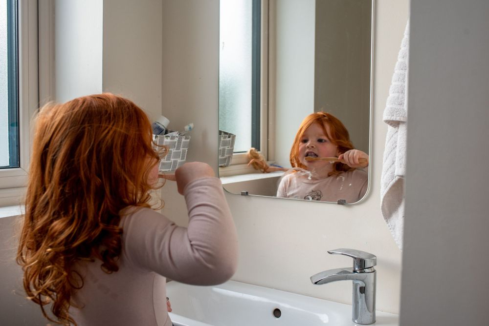 Someone brushing their teeth at a bathroom sink with a mirror.