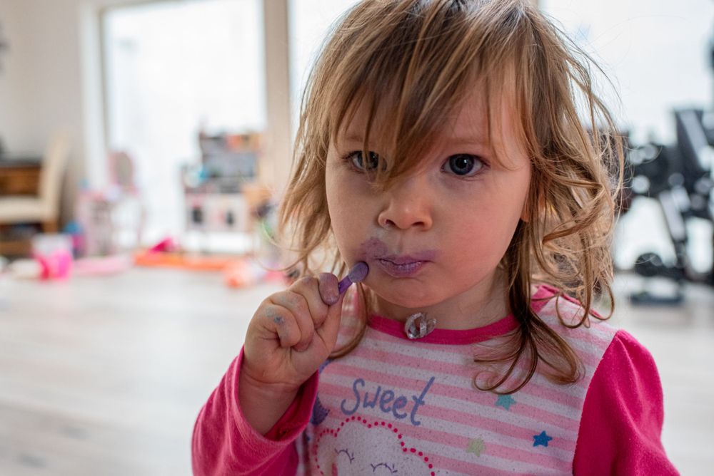 A young toddler in a pink shirt eats a snack.