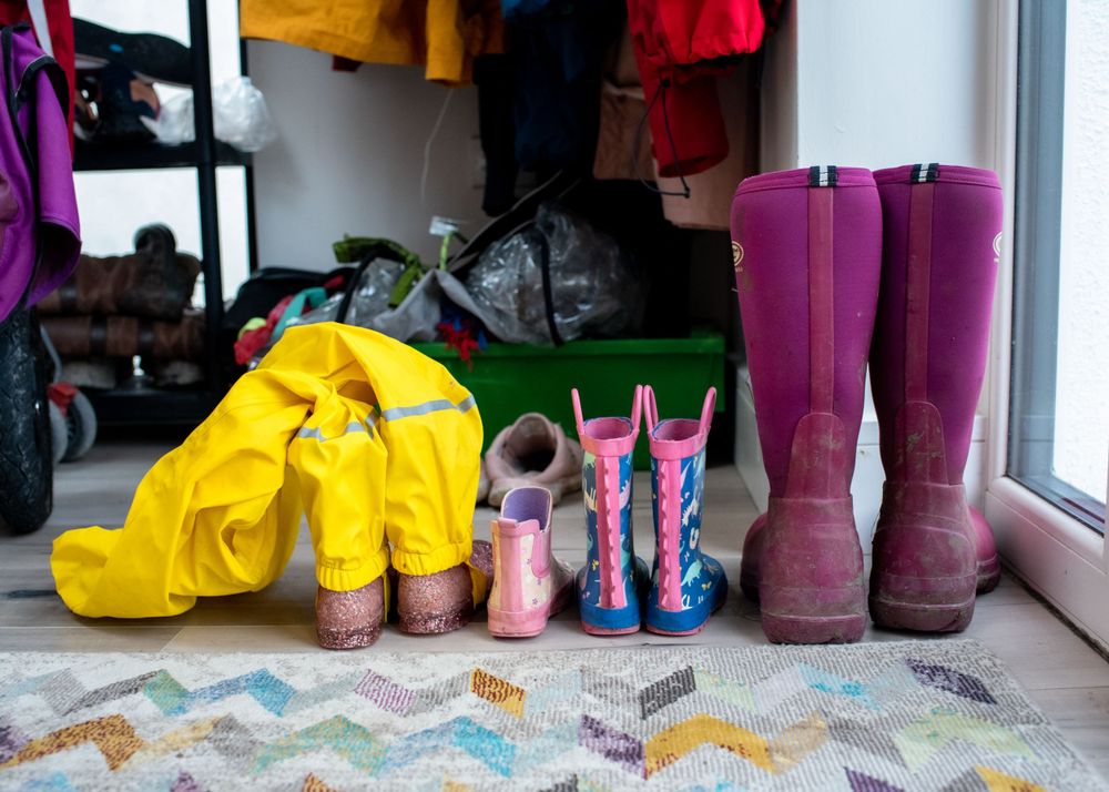 Collection of colorful rain boots lined up by a window on a patterned rug.