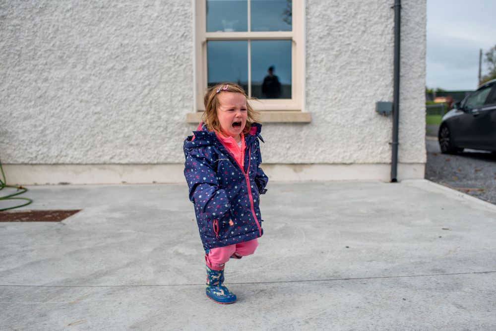 Child in navy patterned jacket jumping excitedly on concrete patio.