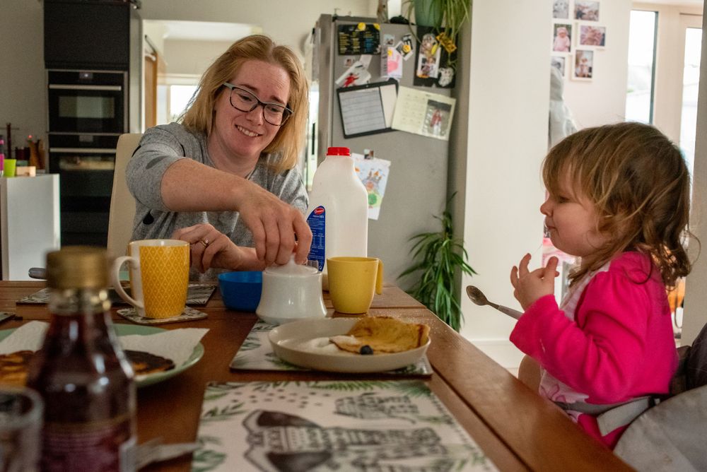 Family having breakfast together at a wooden table with newspapers and drinks.