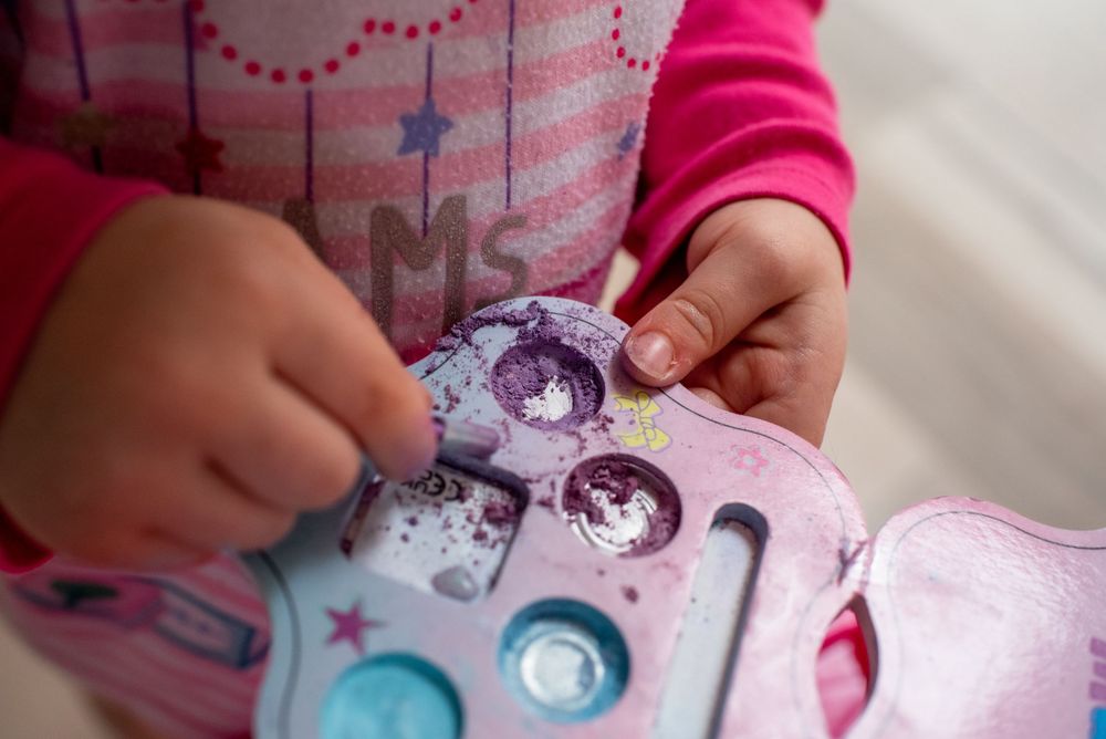 Close-up view of small hands playing with a colorful sparkly sticker or toy.