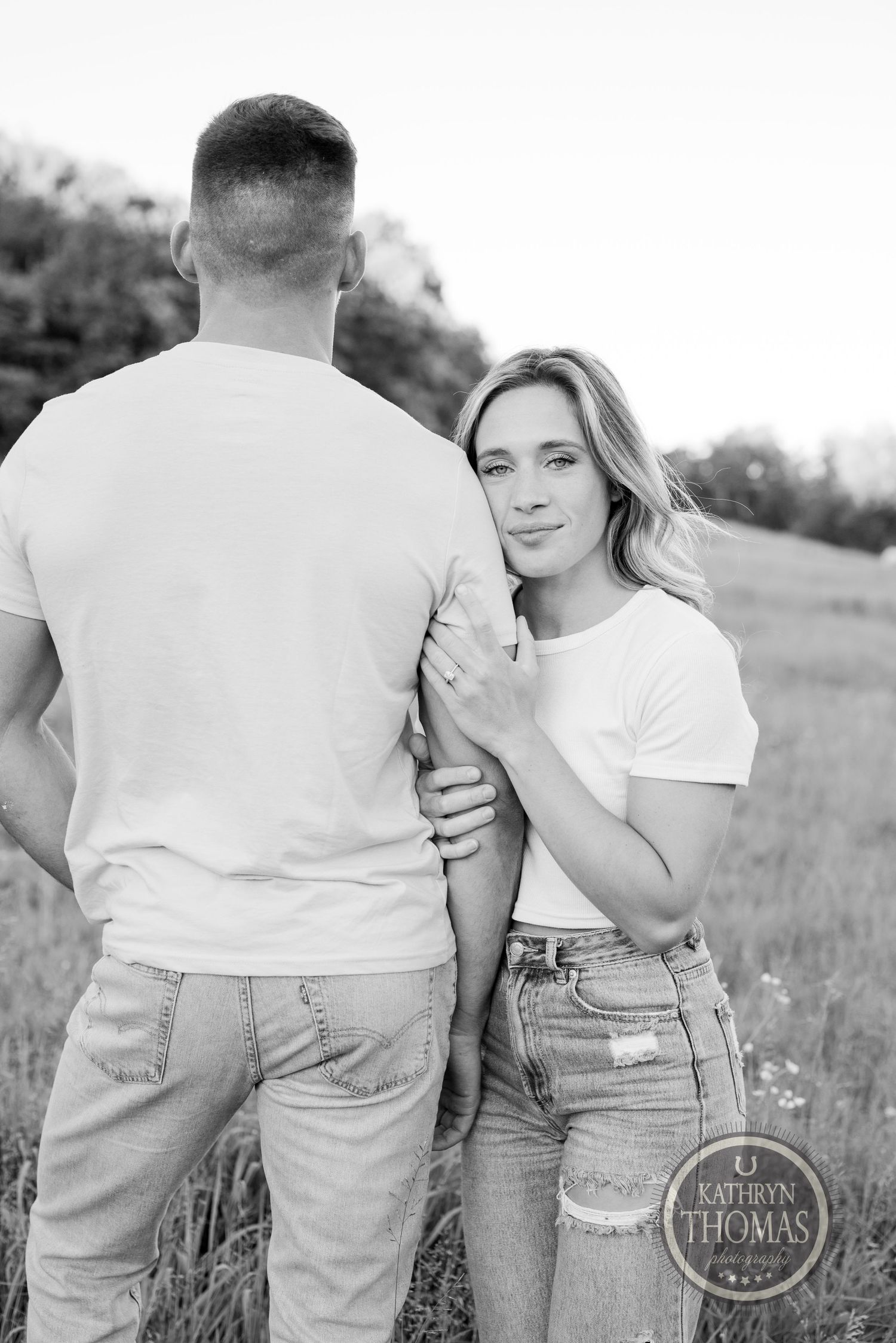 Black and white photo of couple in casual wear standing together in field.