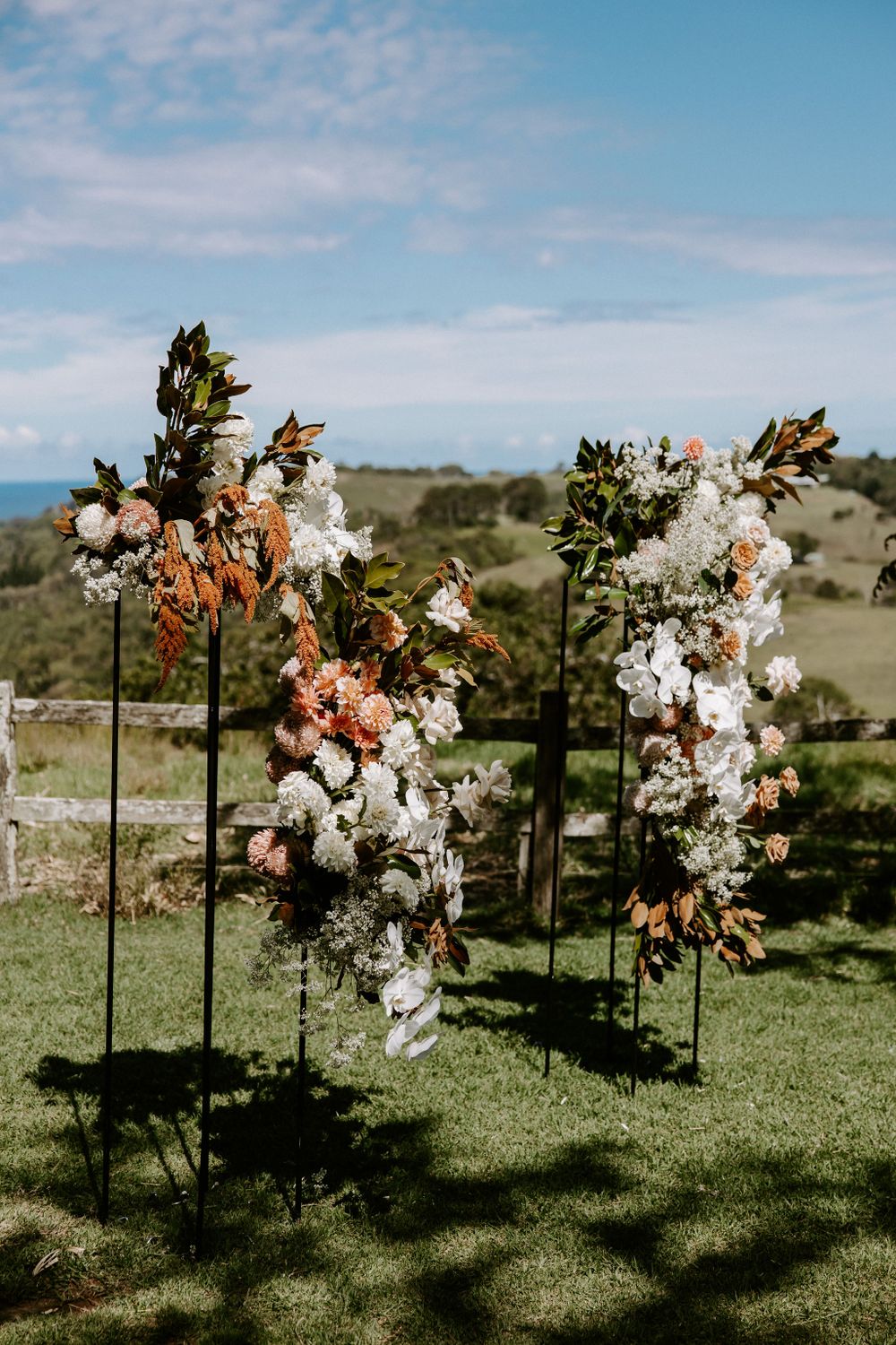 Romantic floral arch with white and peach blooms against rolling hills landscape.