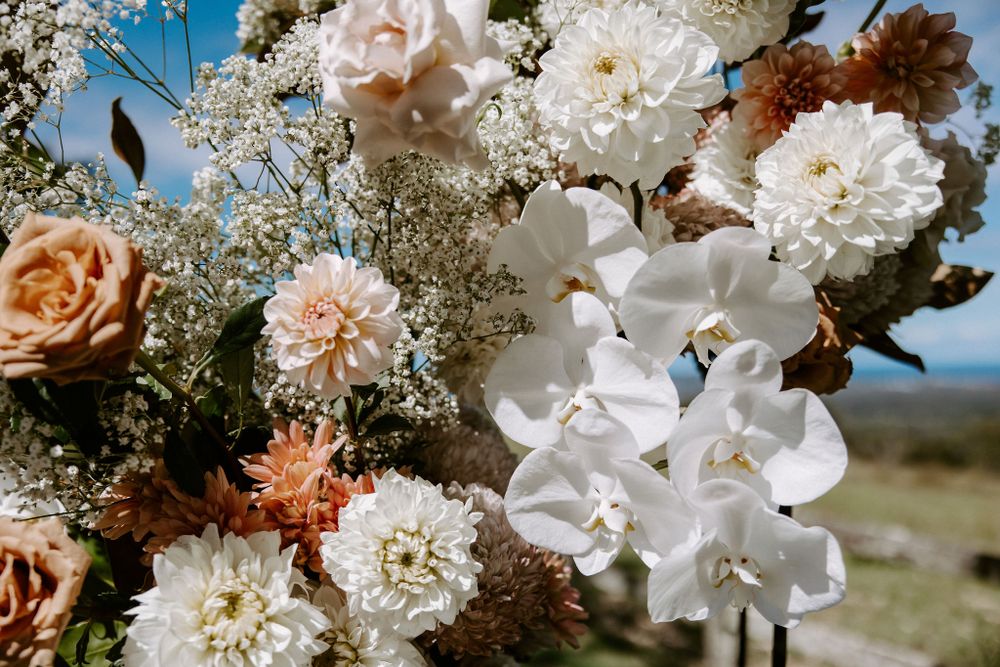 Elegant wedding flower arrangement featuring white orchids, roses and baby's breath in natural sunlight.