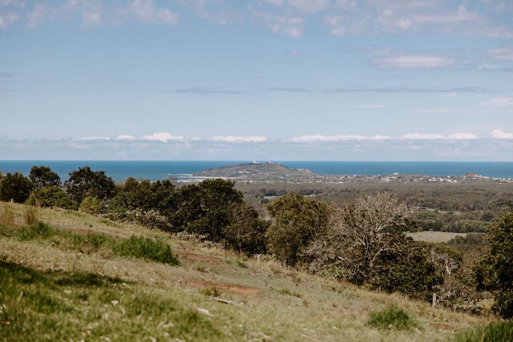 Scenic coastal landscape with rolling hills, ocean views and scattered trees under blue skies.