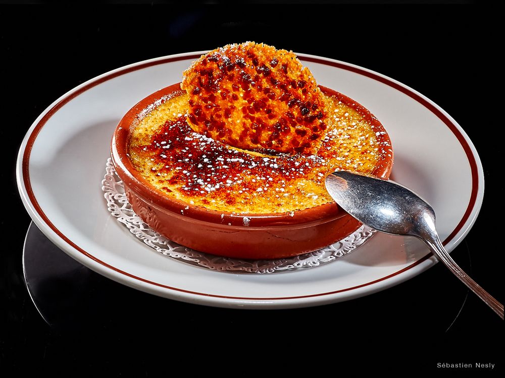 Series of caramelized crème brûlée desserts with burnt sugar tops on white plates with red trim.