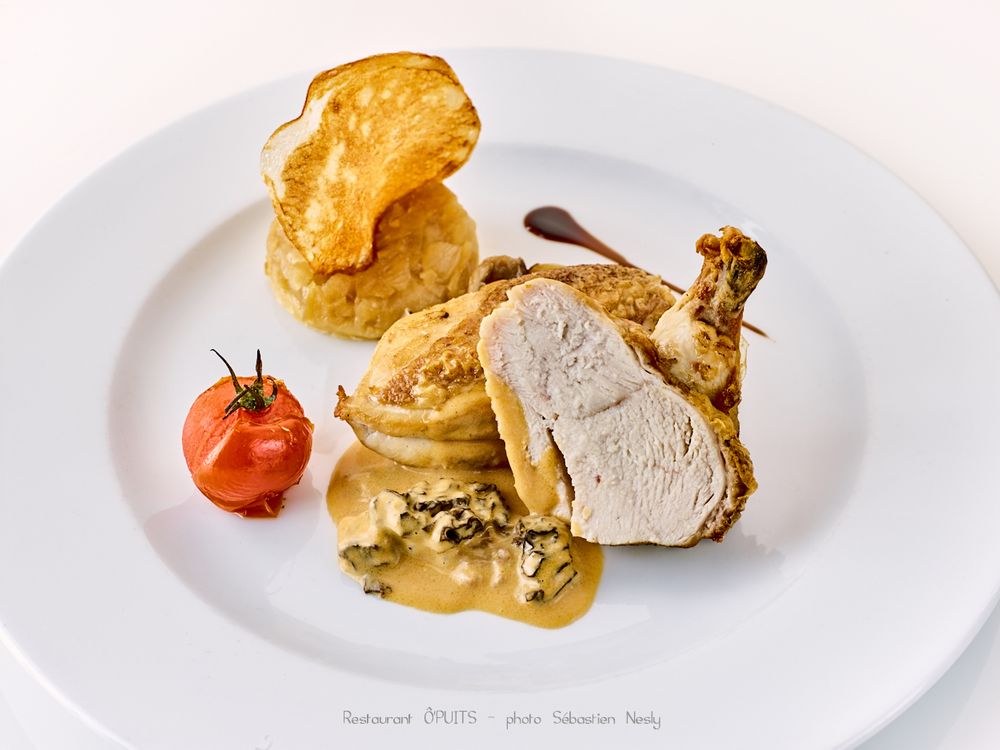 Roasted poultry dish with golden pastry and sauce on white plate.