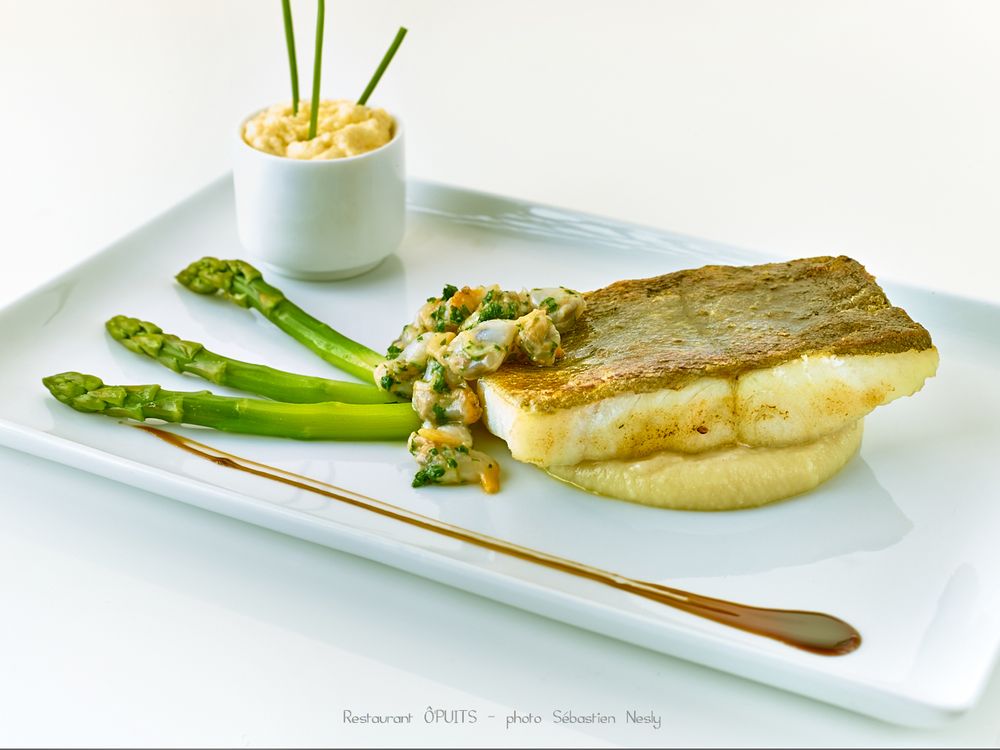 Pan-seared fish with asparagus and cream sauce plated on white rectangular dish.