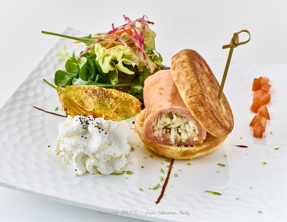Gourmet appetizer with red garnish and microgreens served on white rectangular plate.