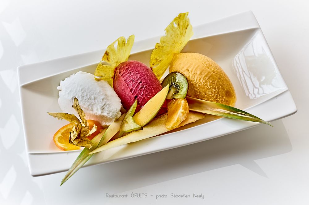 Artfully plated dessert with yellow flower garnish, red fruit and caramel sauce on white rectangular plate.