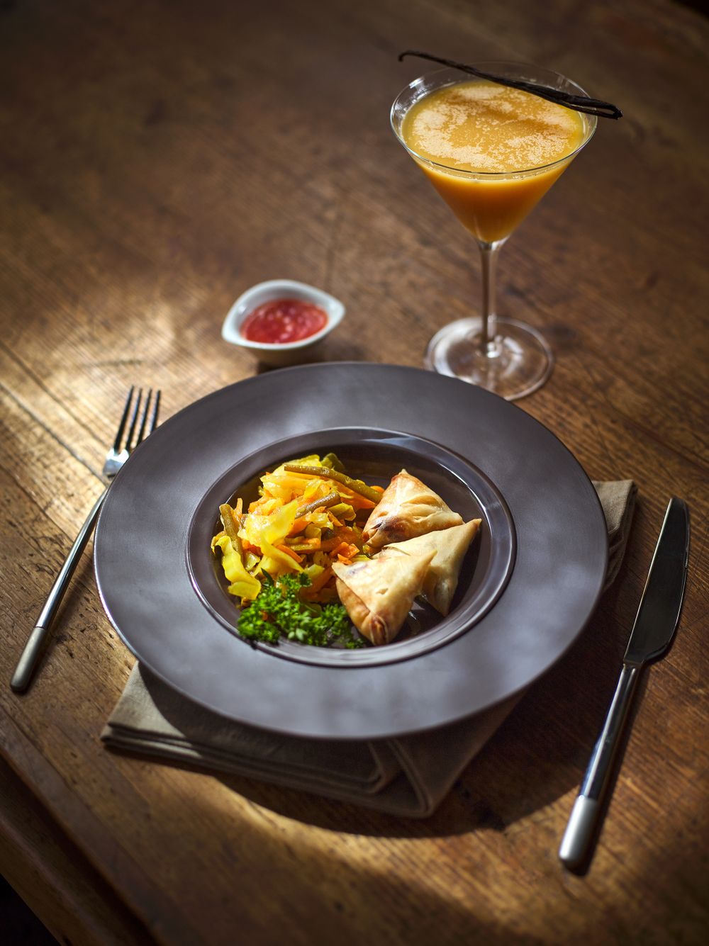 Elegant plated dishes with garnishes served on dark plates against a rustic wooden table.