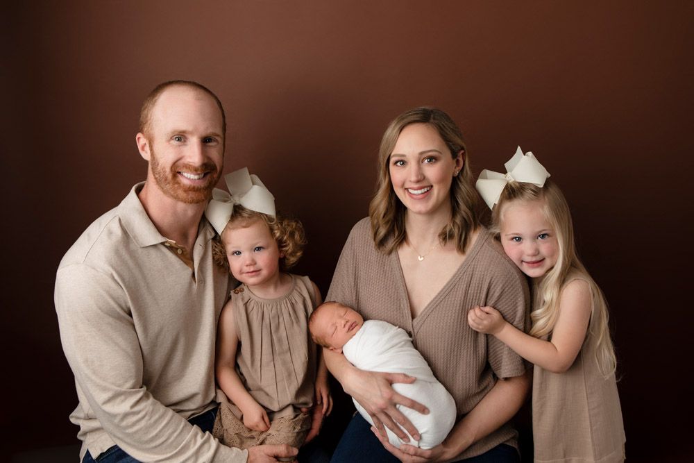 Family of five poses in coordinating neutral tones against brown backdrop.