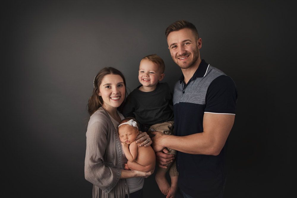 Professional studio portrait of a young family of three against a dark background.