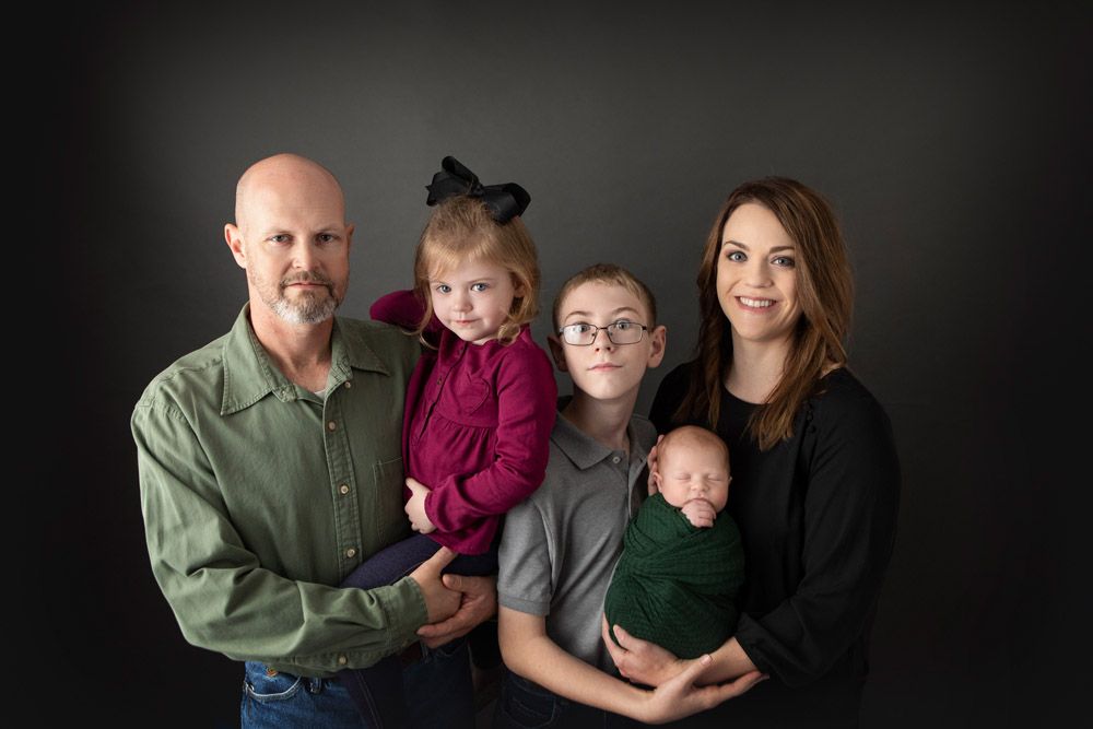 Professional family portrait with four members and infant against dark background.