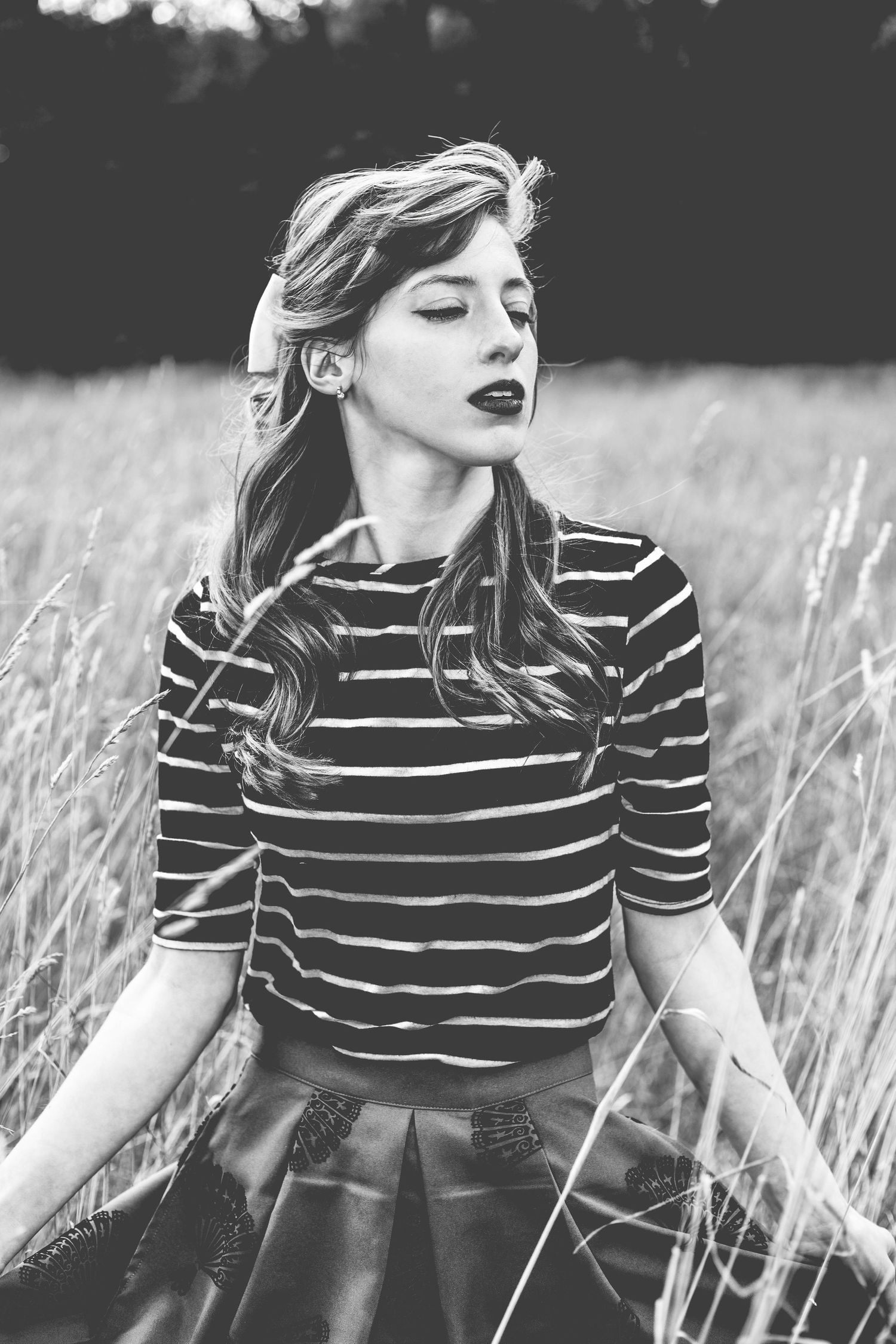 Black and white portrait of a woman in a striped shirt standing in a field of tall grass.