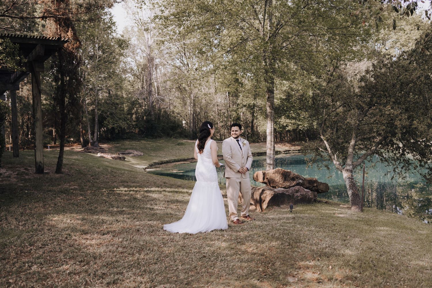 Wedding ceremony takes place next to a serene turquoise pond with natural woodland backdrop.