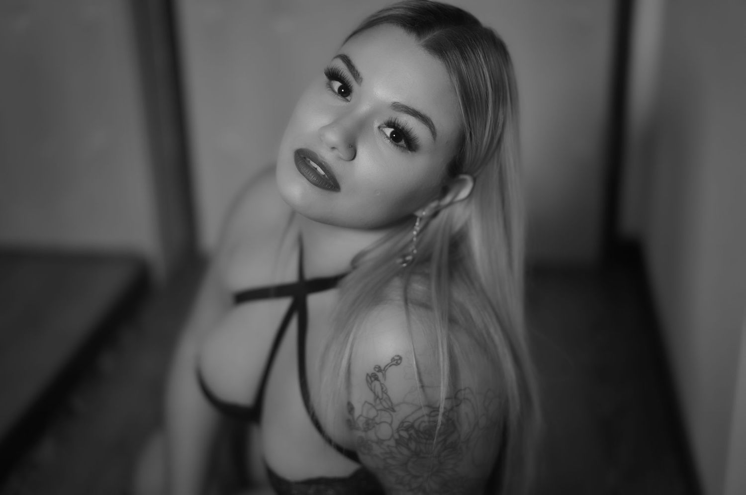 Dramatic black and white portrait showing dark lingerie and artistic shoulder tattoo.