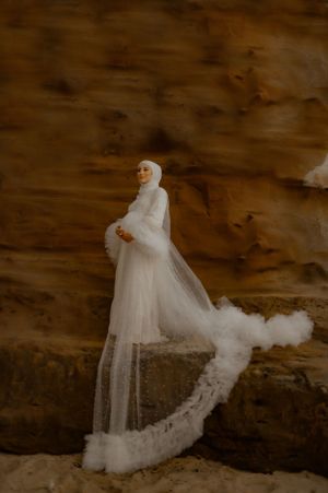 A dramatic bridal portrait showcases a flowing white dress against textured sandstone cliffs.
