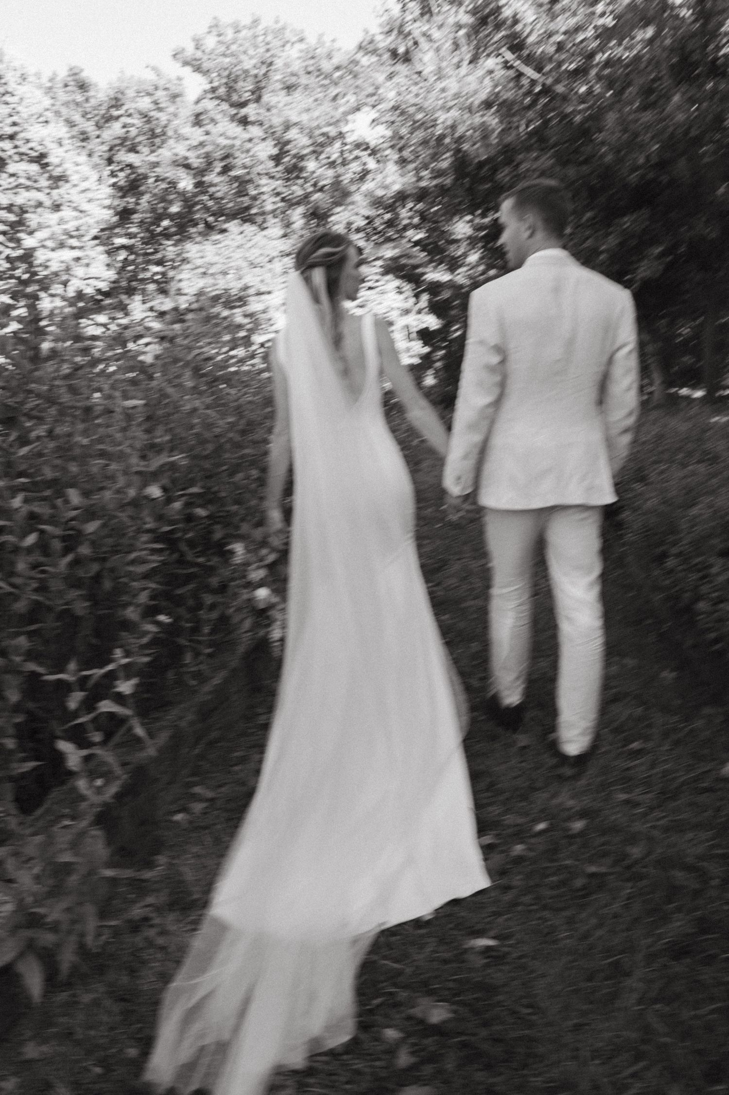 Black and white photo of a newlywed couple walking through a garden path.