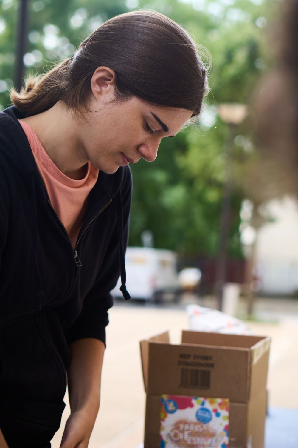 Person in black jacket looking down at a cardboard box outdoors.